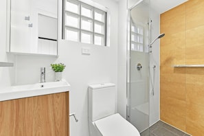 A modern bathroom with a white toilet, a glass-enclosed shower, and a wooden vanity. - Modern Fully Furnished Studio Kingsford (Kingsford)