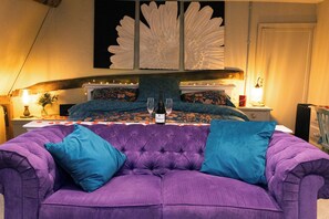Quarto com uma cama grande, sofá roxo e um objeto decorativo na parede.