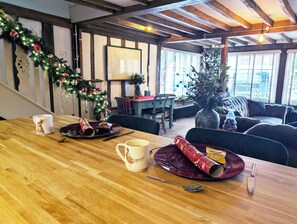 A dining area with a wooden table set for two, a Christmas tree, and a cozy seating area with a couch and chairs. - Chinnerys Country Cottage (Cavendish)