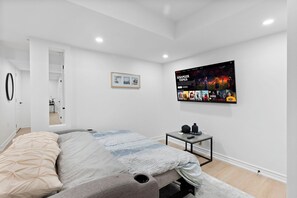Un dormitorio moderno con una cama, una mesita de noche, un cuadro enmarcado y un televisor de pared mostrando una película.