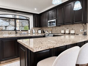 A kitchen with dark cabinets, granite countertops, a built-in microwave, and a large island with seating. - Beautiful "Villa De Familia" Partial Ocean View (Baja California Sur)