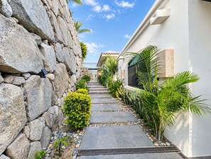 A stone wall, a pathway with plants, and a building with a window. - Beautiful "Villa De Familia" Partial Ocean View (Baja California Sur)