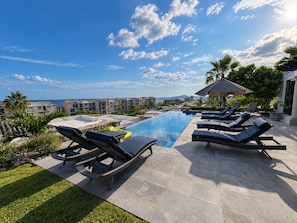 Uma área à beira da piscina com espreguiçadeiras, uma piscina pequena e vista para uma zona residencial com edifícios e montanhas ao longe.
