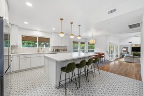 A modern kitchen with a central island, bar stools, pendant lighting, and a view of the outdoors.