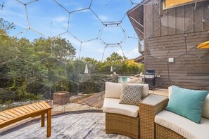 A patio with outdoor furniture, a wooden table, and a barbecue grill. - Toro Haus: Secluded Pool & Pickleball Paradise (Austin)