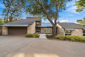 A modern two-story house with a garage, stone exterior, and a large tree in front. - Toro Haus: Secluded Pool & Pickleball Paradise (Austin)