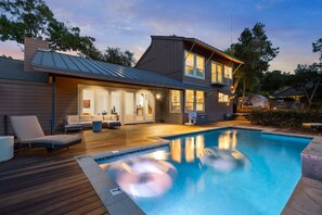 A two-story house with a swimming pool, outdoor seating, and a large window overlooking the pool.