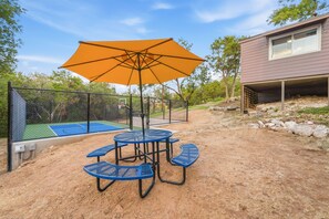 An outdoor patio with a table and chairs, a basketball court, and a covered area with an umbrella.