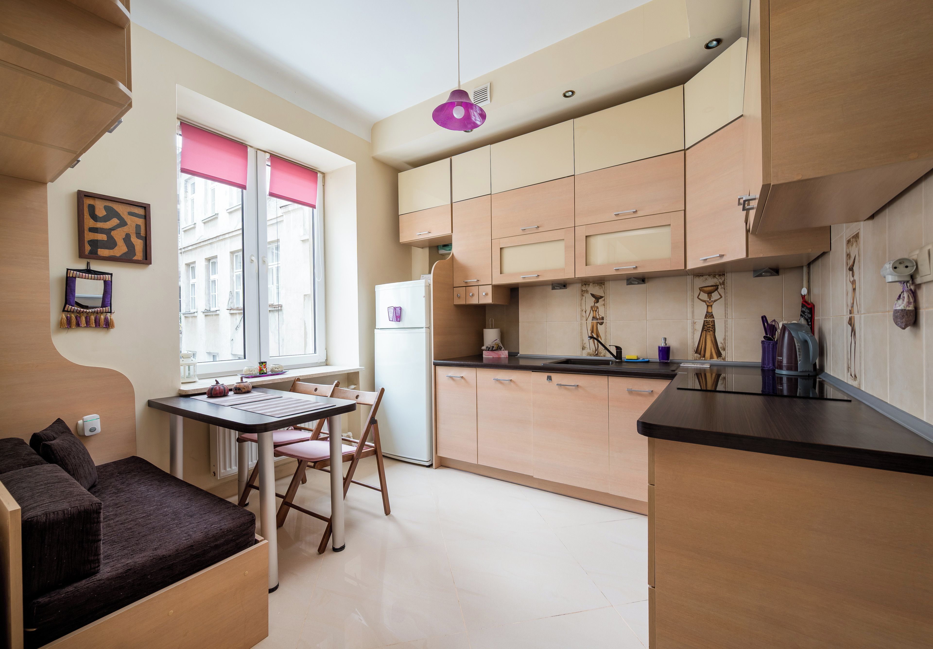 A compact kitchen with a dining area, featuring a refrigerator, cabinets, and a window with blinds.
