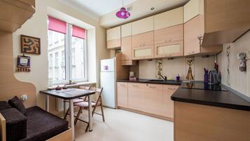 A compact kitchen with a dining area, featuring a refrigerator, cabinets, and a window with blinds.