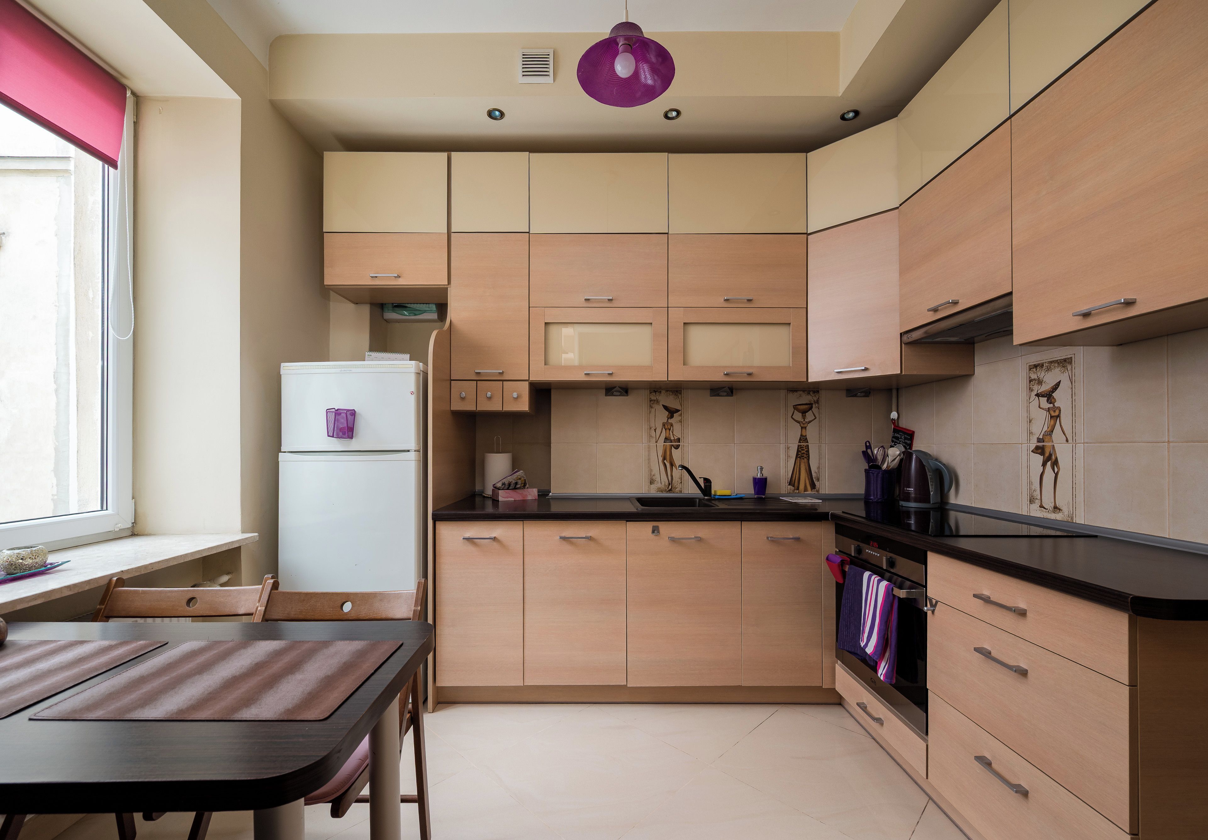 A compact kitchen with wooden cabinets, a refrigerator, and a dining area with a table and chairs.
