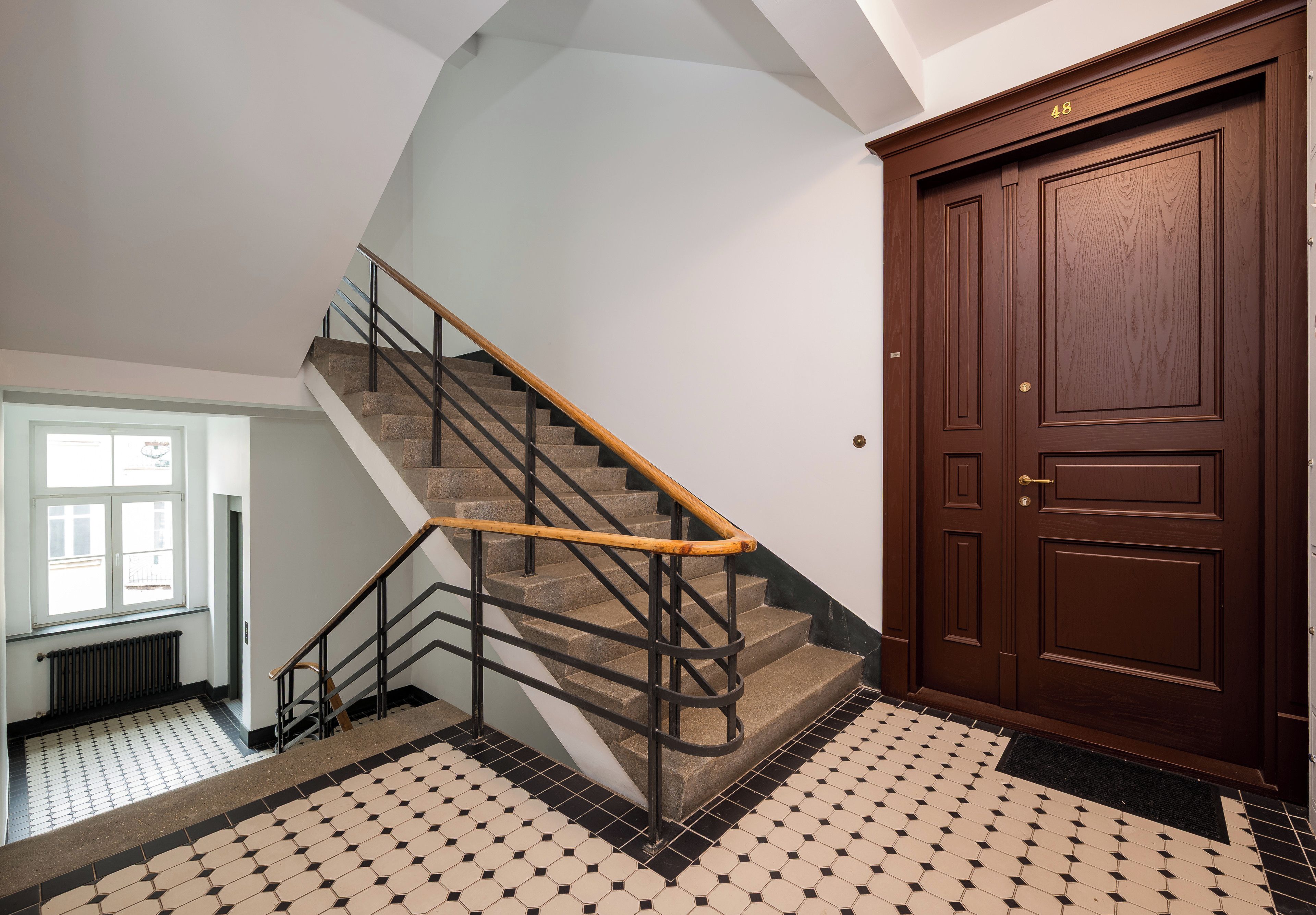 A staircase with a wooden handrail and black metal railings, leading to a door with a brass handle.