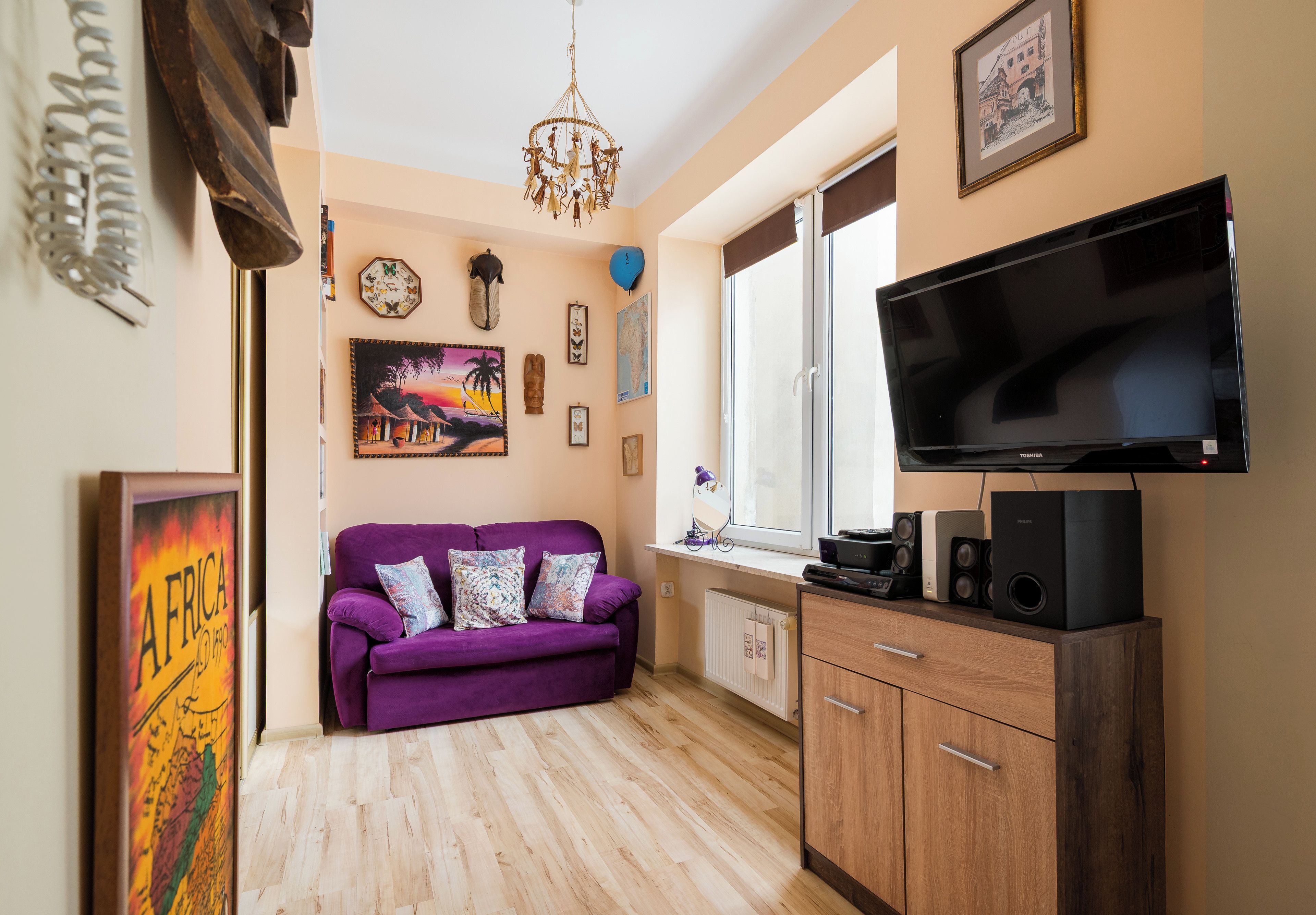 Una sala de estar con un sofá púrpura, un televisor de pantalla plana, armarios de madera y diversas decoraciones en las paredes.