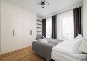 Ein Schlafzimmer mit einem Bett, einem Kleiderschrank, einem Sessel und einem Fenster mit Vorhängen.