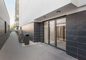 A narrow alley with a row of bicycles parked on the left, a trash bin, and a building entrance with a glass door. - Marymont Superior Apartment (Warszawa)