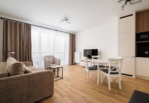 A modern living room with a sofa, a dining table with chairs, a television, and a kitchen area. - Marymont Superior Apartment (Warszawa)