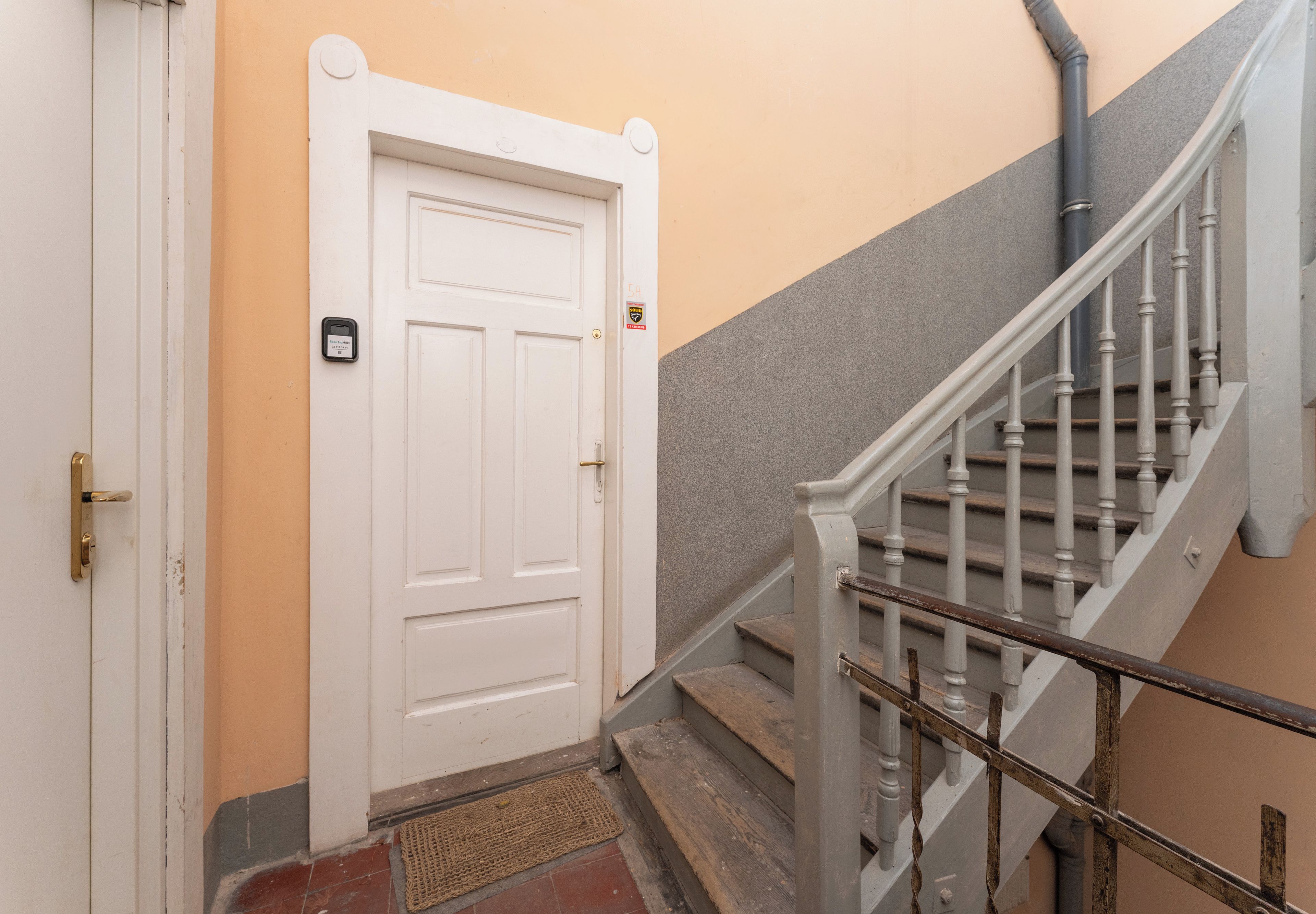Una scala con corrimano, una porta bianca con campanello e un tappetino d'ingresso.