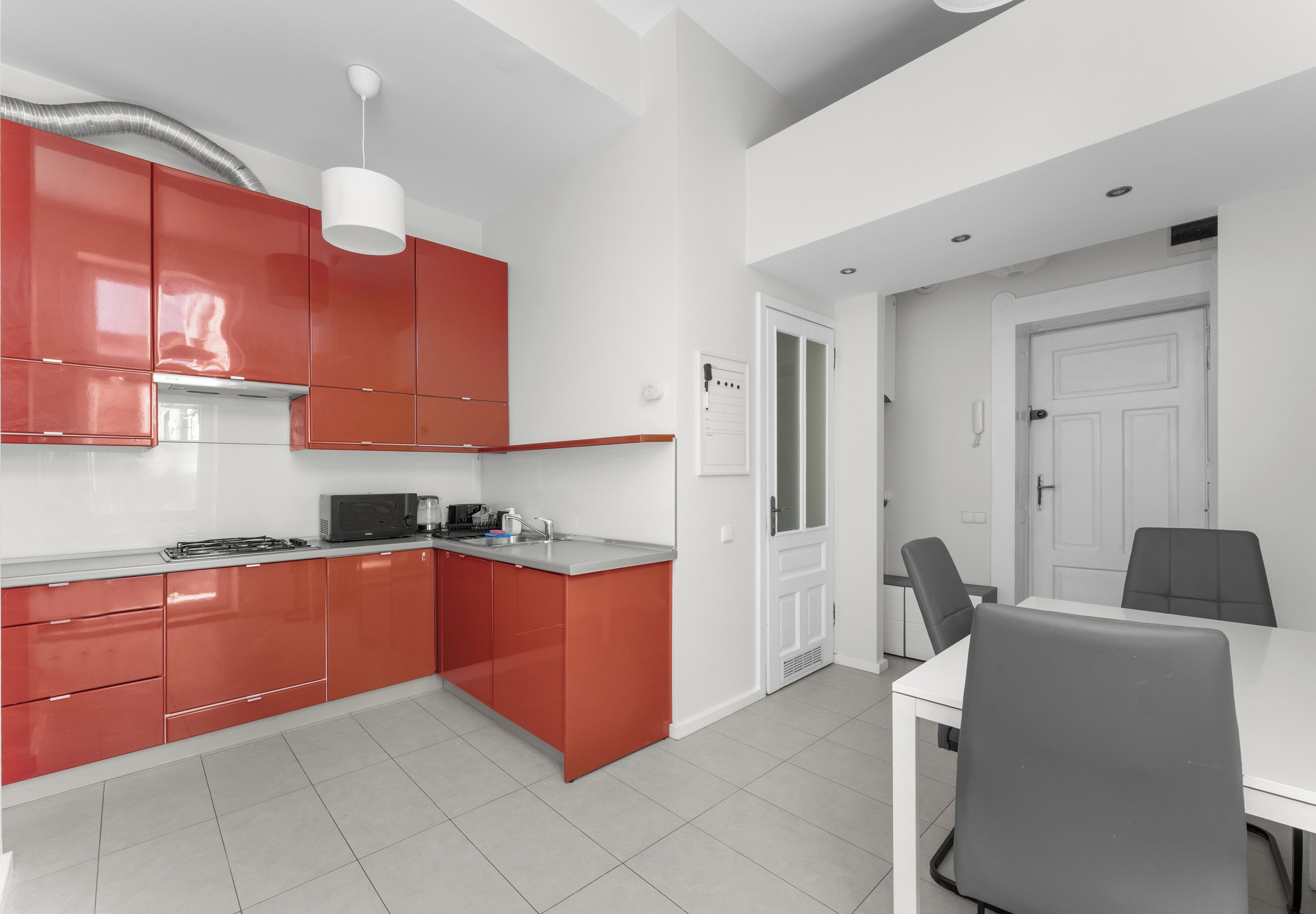 A modern kitchen with red cabinets, a white countertop, and a dining area with a table and chairs.