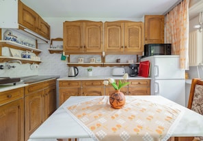 A kitchen with wooden cabinets, a microwave, a toaster, and a table with a floral tablecloth. - Piaskowa 57 Homely Apartment (Police)