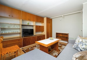 A compact living space with wooden cabinets, a flat-screen TV, a dining table, and a sofa. - Piaskowa 57 Homely Apartment (Police)