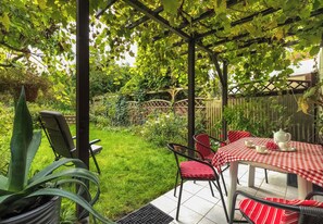 Een overdekt terras met een tafel gedekt voor thee, omringd door stoelen, en een weelderige tuin op de achtergrond.