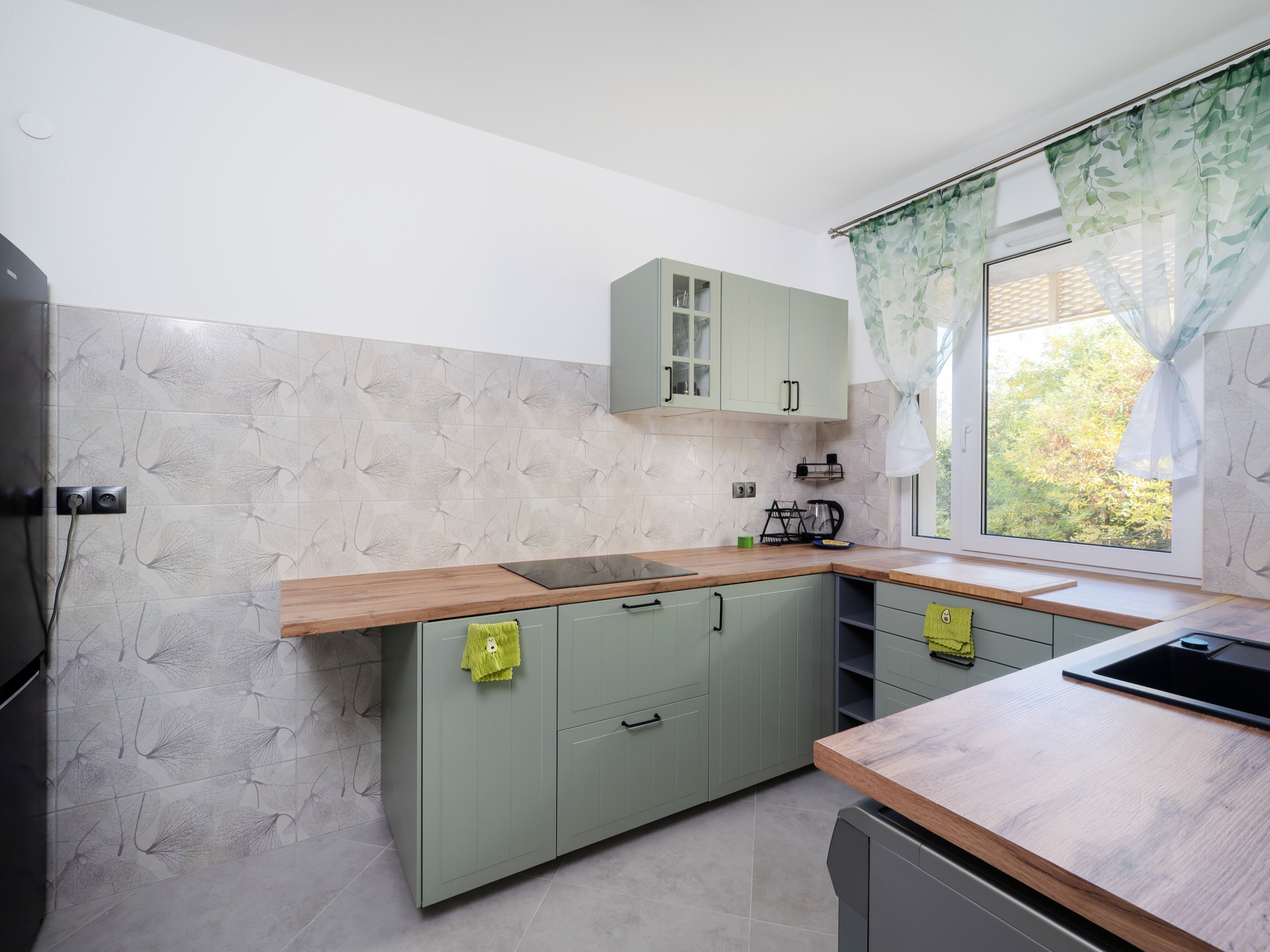 Una cocina con encimera de madera, armarios verdes y una ventana con vistas a la vegetación.
