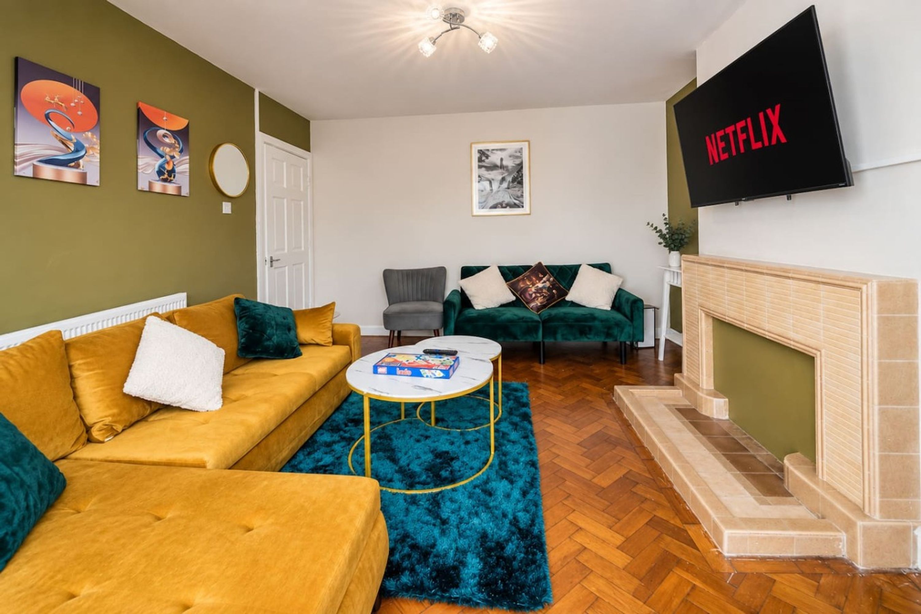 Een woonkamer met een bank, fauteuils, een salontafel, een open haard en een aan de muur bevestigde televisie.
