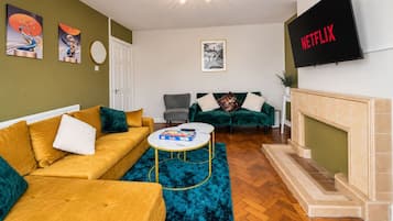 Een woonkamer met een bank, fauteuils, een salontafel, een open haard en een aan de muur bevestigde televisie.