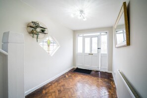 A hallway with a herringbone floor, a white radiator, a door with a window, and a wall-mounted mirror. - Spacious 4BR Sleeps 10 Free Parking (Cardiff)
