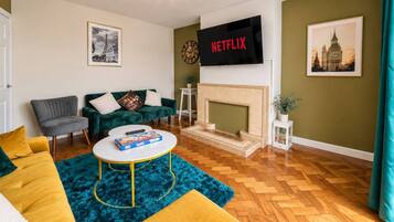 Una sala de estar con un sofá verde, un sillón gris, una mesa de centro, una chimenea y un televisor de pantalla plana montado en la pared.