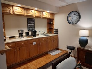 Eine Küche mit Holzschränken, einer Kaffeemaschine, einem Spülbecken und einer Uhr an der Wand.