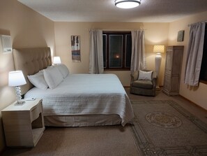 Ein Hotelzimmer mit einem Bett, Nachttischen, einem Sessel, einem Fenster mit Vorhängen, einer Lampe und einer Heizung.