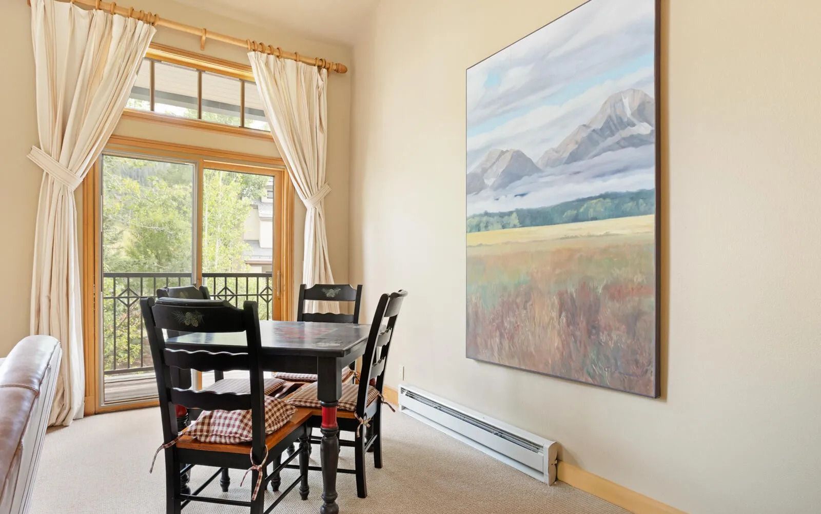 A dining area with a table and chairs, a window with curtains, and a painting on the wall.