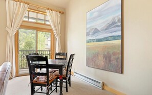 Un coin repas avec une table et des chaises, une fenêtre avec des rideaux et un tableau accroché au mur.