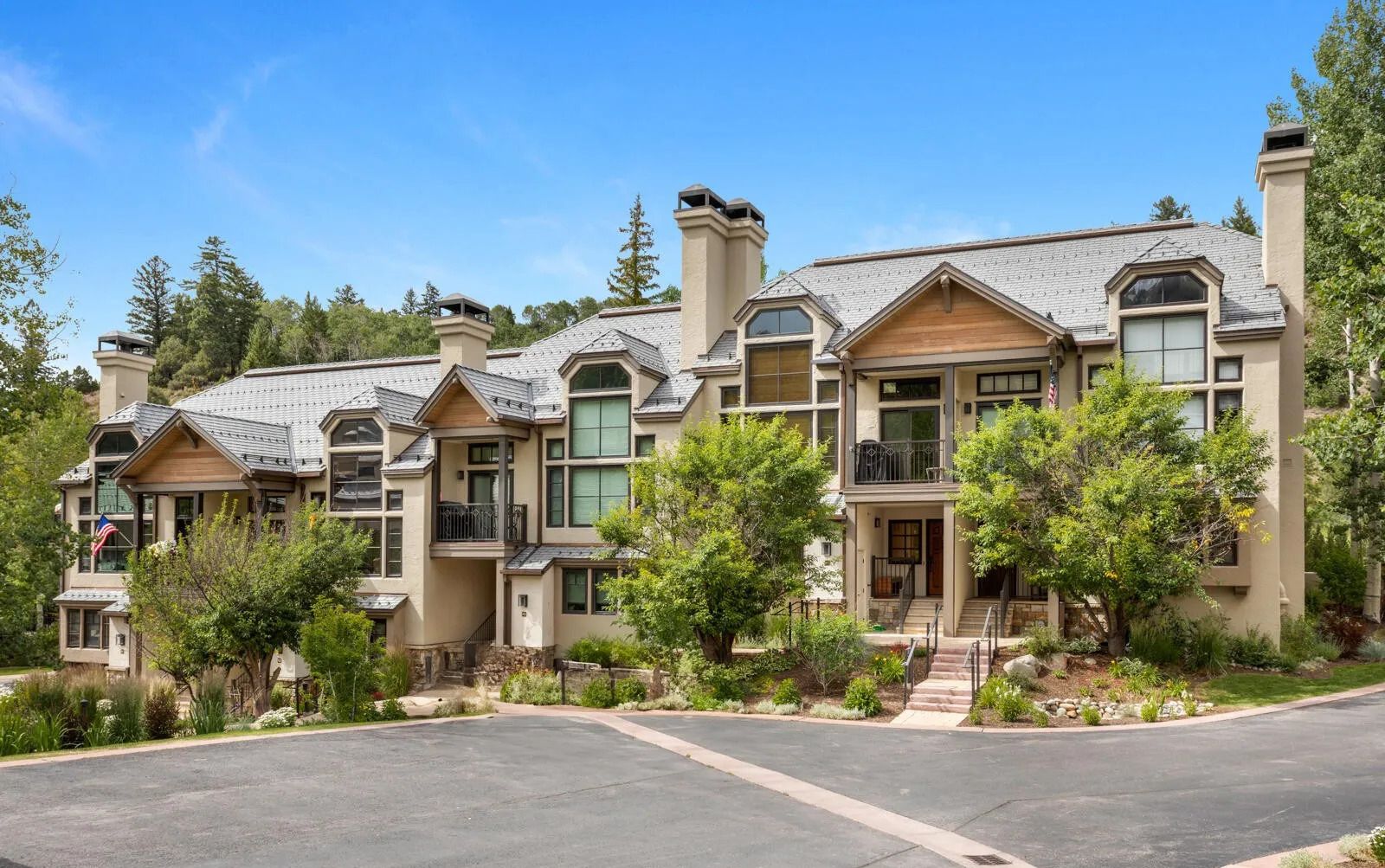 A multi-story residential building with a symmetrical facade, multiple chimneys, and a well-maintained front yard with trees and shrubs.
