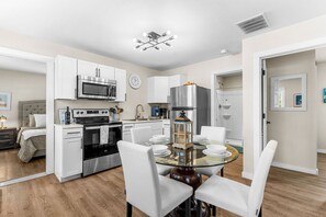 A modern kitchen with white cabinets, a stainless steel oven, and a dining area with a glass table and white chairs. - Table Rock Lakefront Home Near Port of Kimberling_Free Attraction Tickets_Firepit (Kimberling City)