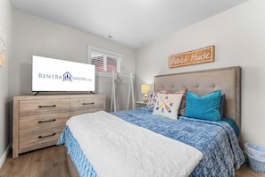 A bedroom with a bed, a dresser, a television displaying a rental company logo, a window with blinds, and a sign that says 'Beach House'. - Table Rock Lakefront Home Near Port of Kimberling_Free Attraction Tickets_Firepit (Kimberling City)