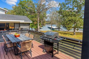 Terraza al aire libre con parrilla, mesa de comedor y sillas, con vista a un cuerpo de agua y barcos amarrados.