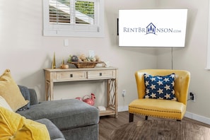 A living room with a sofa, a yellow armchair, a wooden console table, and a television mounted on the wall. - Table Rock Lakefront Home Near Port of Kimberling_Free Attraction Tickets_Firepit (Kimberling City)