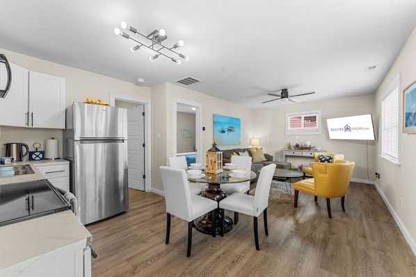 A modern kitchen with a stainless steel refrigerator, a dining area with a glass table and white chairs, and a ceiling fan. - Table Rock Lakefront Home Near Port of Kimberling_Free Attraction Tickets_Firepit (Kimberling City)