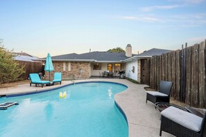 A backyard with a swimming pool, lounge chairs, and a wooden fence. - Prime Location | Pool | Game Room | King Bed (Plano)