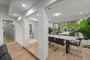 A modern interior with a dining area, white brick columns, and a view through large windows. - Prime Location | Pool | Game Room | King Bed (Plano)