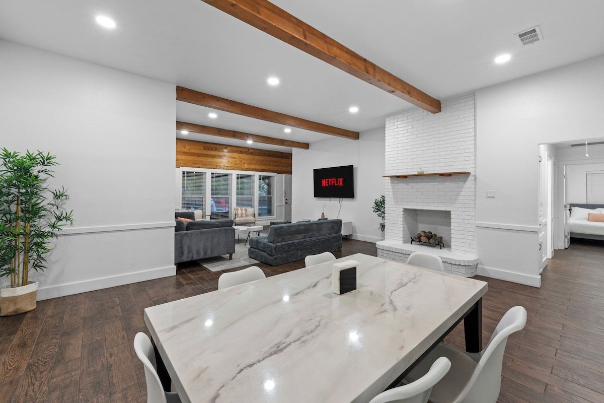 A modern living room with a fireplace, a dining area with a marble table, and a television mounted on the wall.