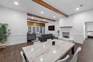 A modern living room with a fireplace, a dining area with a marble table, and a television mounted on the wall. - Modern House I Huge Yard I Pool I Cinema & Game Room (Denton)