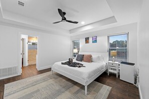 Une chambre à coucher avec un lit, des tables de chevet, un radiateur, un ventilateur de plafond et une vue par la fenêtre.