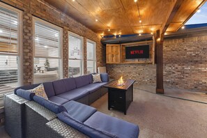 An outdoor seating area with a sofa, a fire pit, and a wall-mounted TV displaying 'NETFLIX'. - Modern House I Huge Yard I Pool I Cinema & Game Room (Denton)