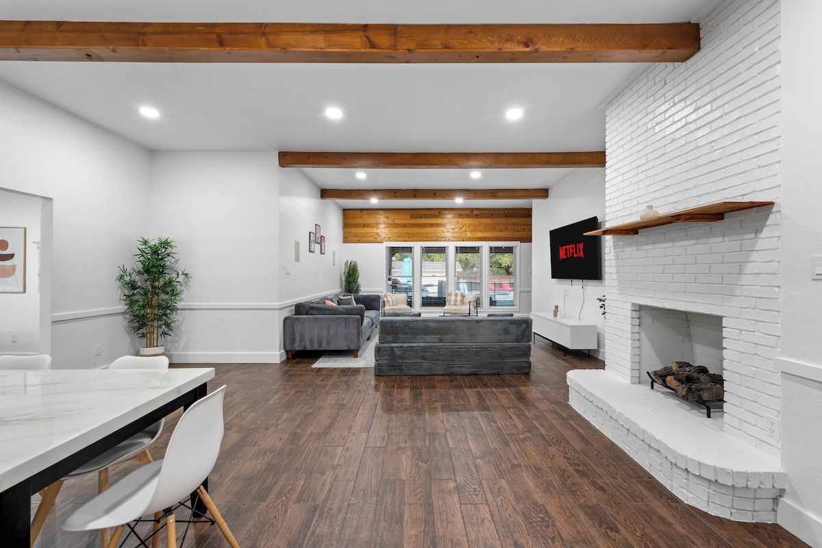 A modern living room with a fireplace, a sofa, a TV, and a dining area with a table and chairs.