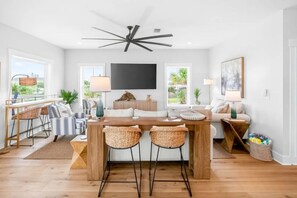 A modern living room with a wooden coffee table, striped chairs, a sofa, and a TV mounted on the wall. - Luxe 6BR Heated Pool | 200 Ft to Beach | Sleeps 20 (gulf shores)