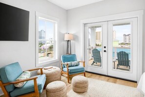 A modern living room with a blue armchair, a floor lamp, and a view of a pool and buildings through large sliding doors. - Luxe 6BR Heated Pool | 200 Ft to Beach | Sleeps 20 (gulf shores)