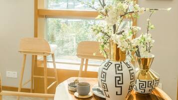 Una mesa de madera con un jarrón de flores, una taza y un platillo. Hay dos sillas y una escalera apoyada en la pared.